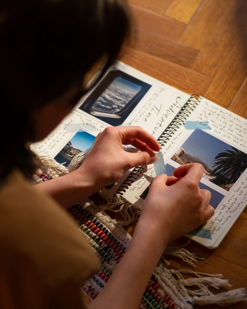 Main d'une femme collant des photos dans un carnet de voyage, illustrant la créativité et le storytelling visuel pour la communication numérique.