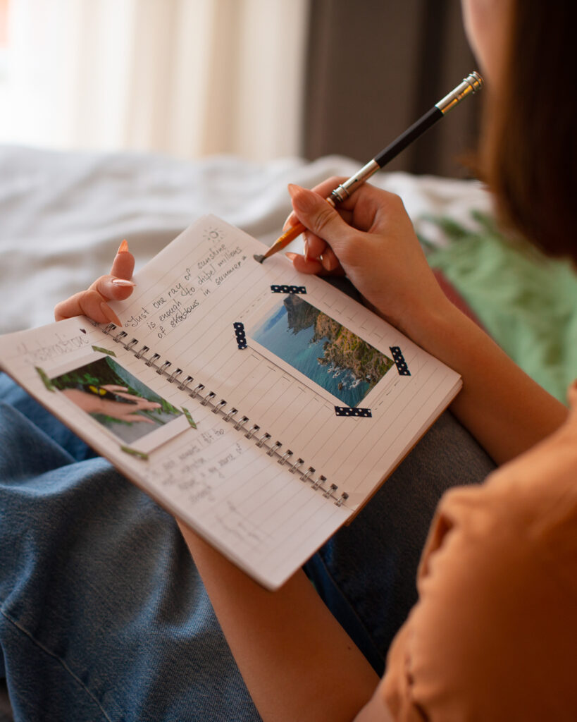 Femme écrivant dans un carnet avec des photos de paysages, symbole de la planification stratégique et du storytelling personnalisé pour une communication digitale impactante